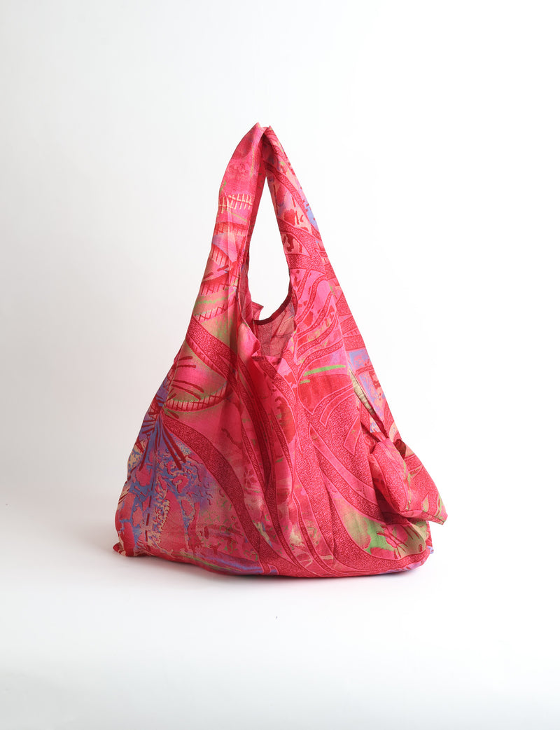 Blue reusable bag with tropical floral pattern in pink, yellow, and green, shown hanging with handles visible