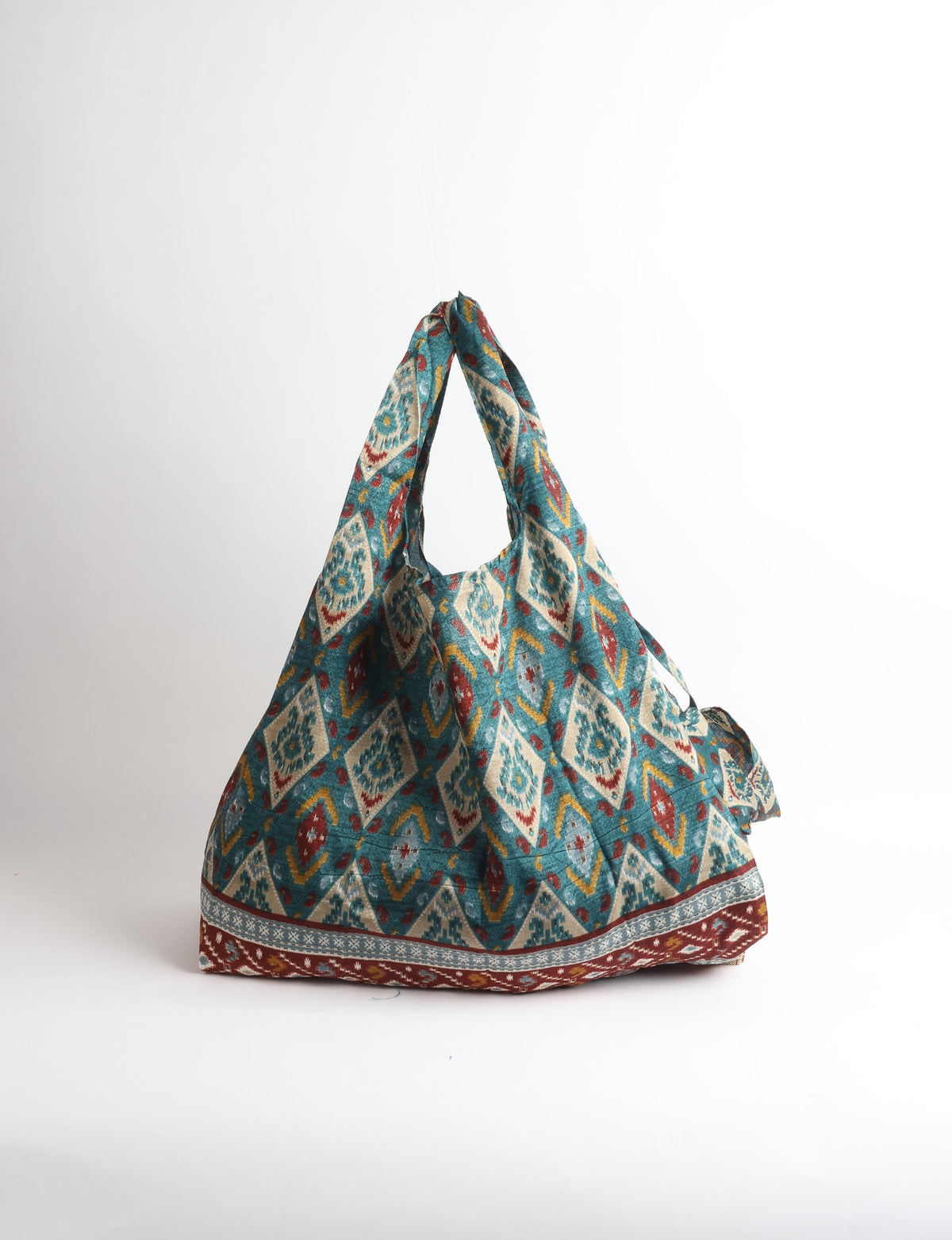 Blue reusable bag with tropical floral pattern in pink, yellow, and green, shown hanging with handles visible