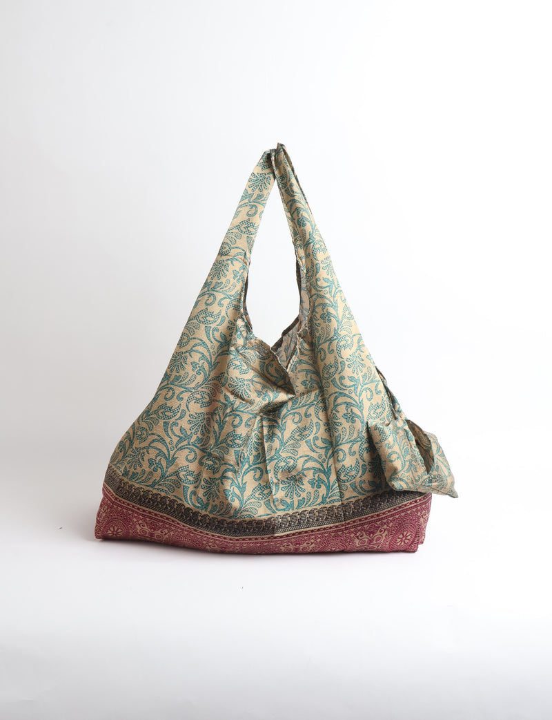 Blue reusable bag with tropical floral pattern in pink, yellow, and green, shown hanging with handles visible