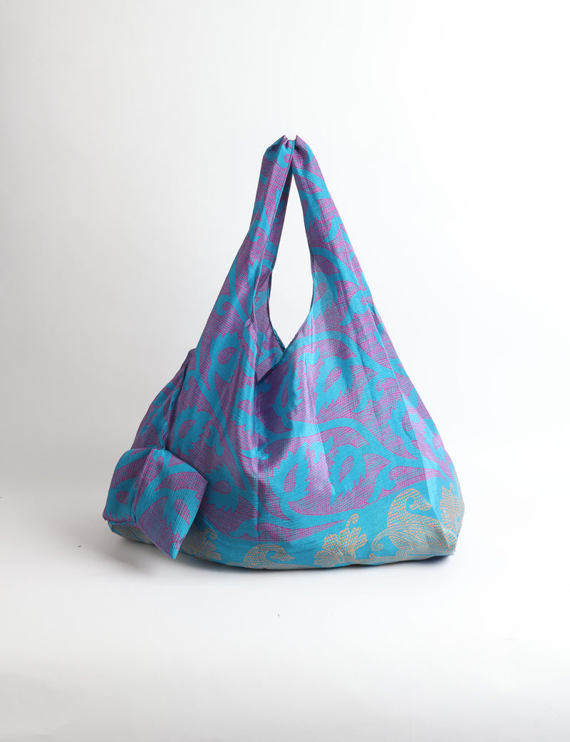Blue reusable bag with tropical floral pattern in pink, yellow, and green, shown hanging with handles visible