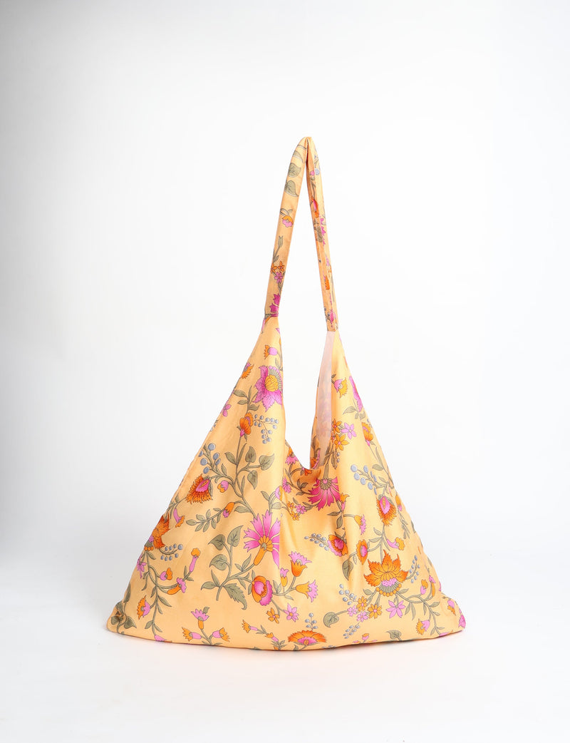 Yellow floral trapeze bag with pink, orange, and green flower patterns, shown front view hanging by straps