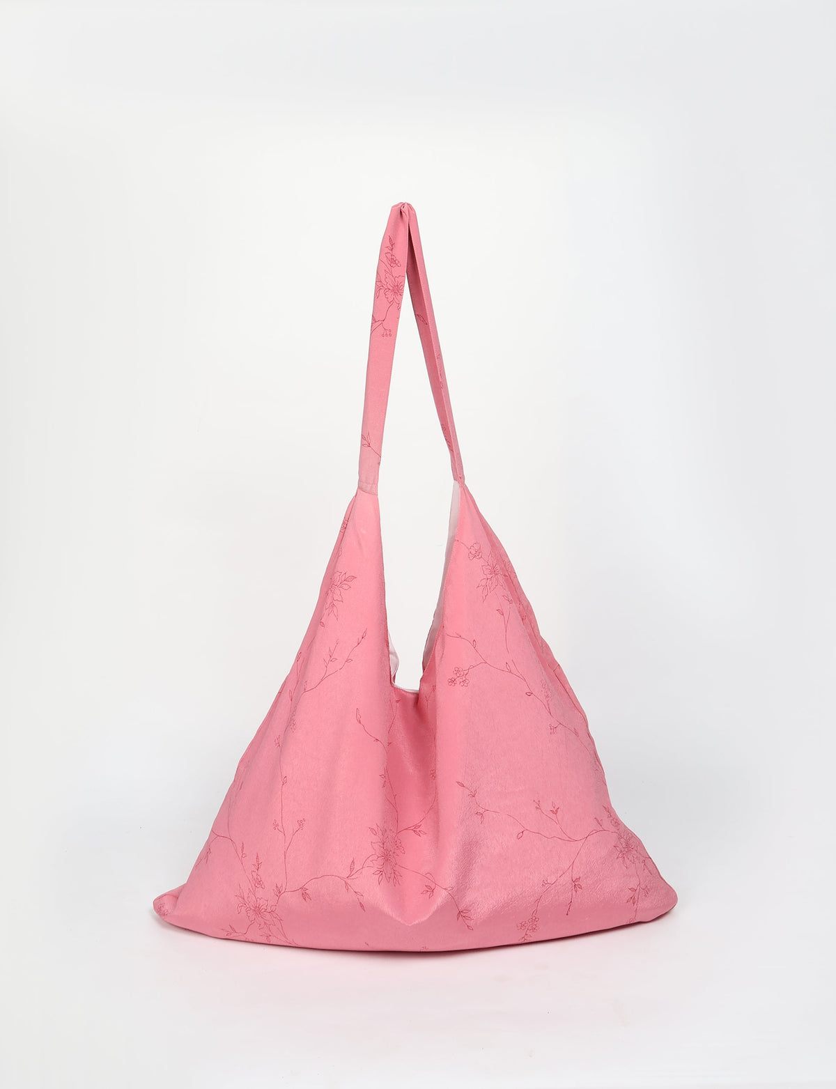 Pink trapeze bag with subtle floral line pattern, soft fabric, and long shoulder strap, shown front view on white background