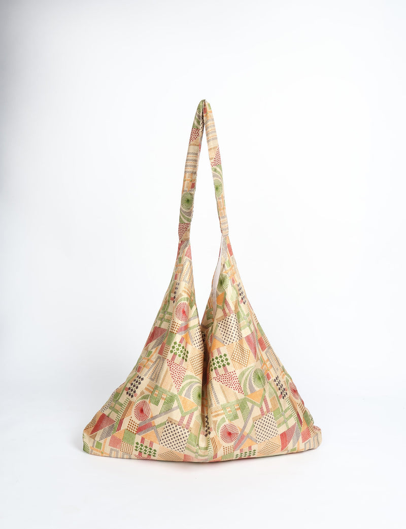 Beige trapeze bag with geometric pattern in green, orange, red, and brown, shown front view hanging by straps
