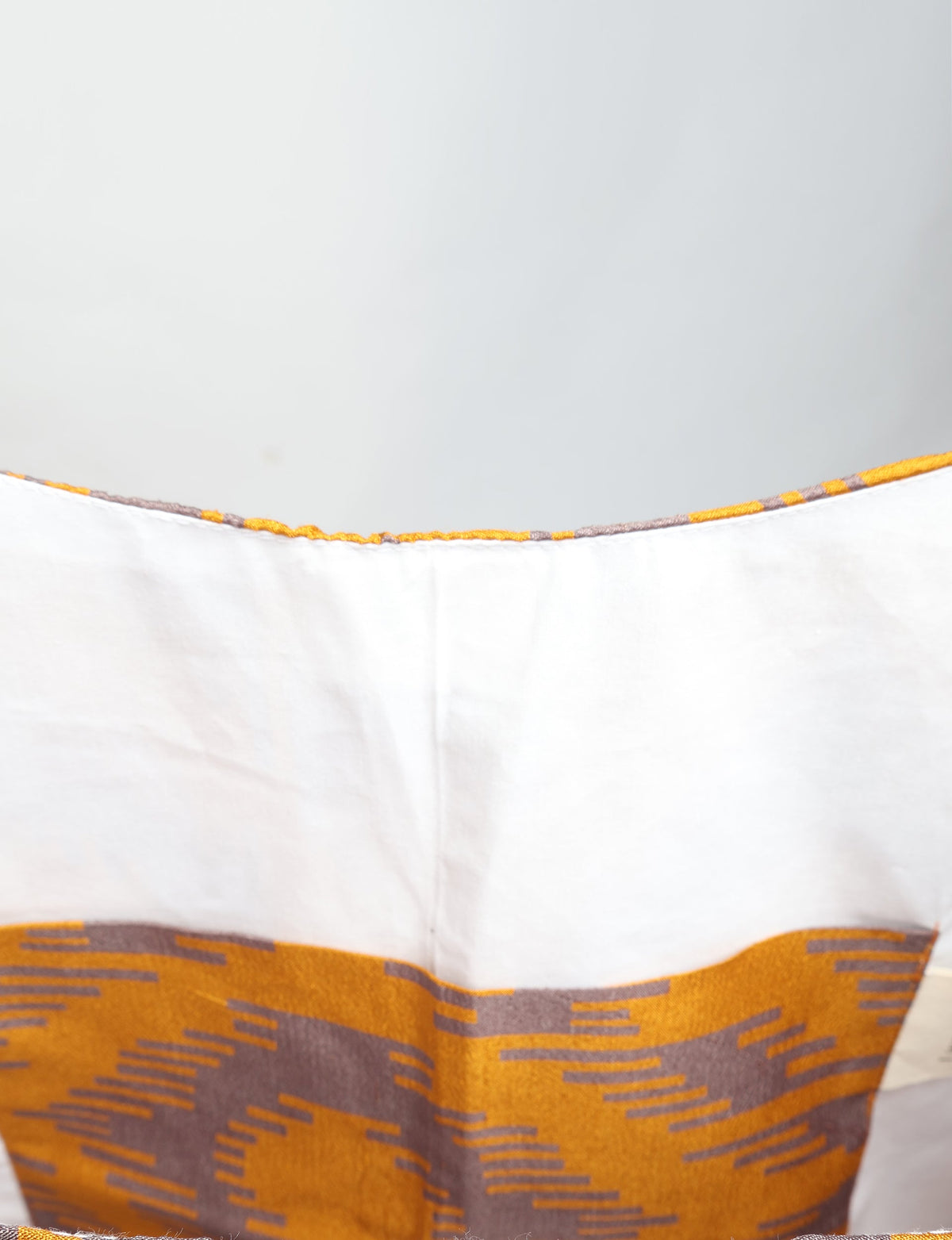 Yellow and brown ikat patterned trapeze bag with white fabric top edge, shown in close-up front view