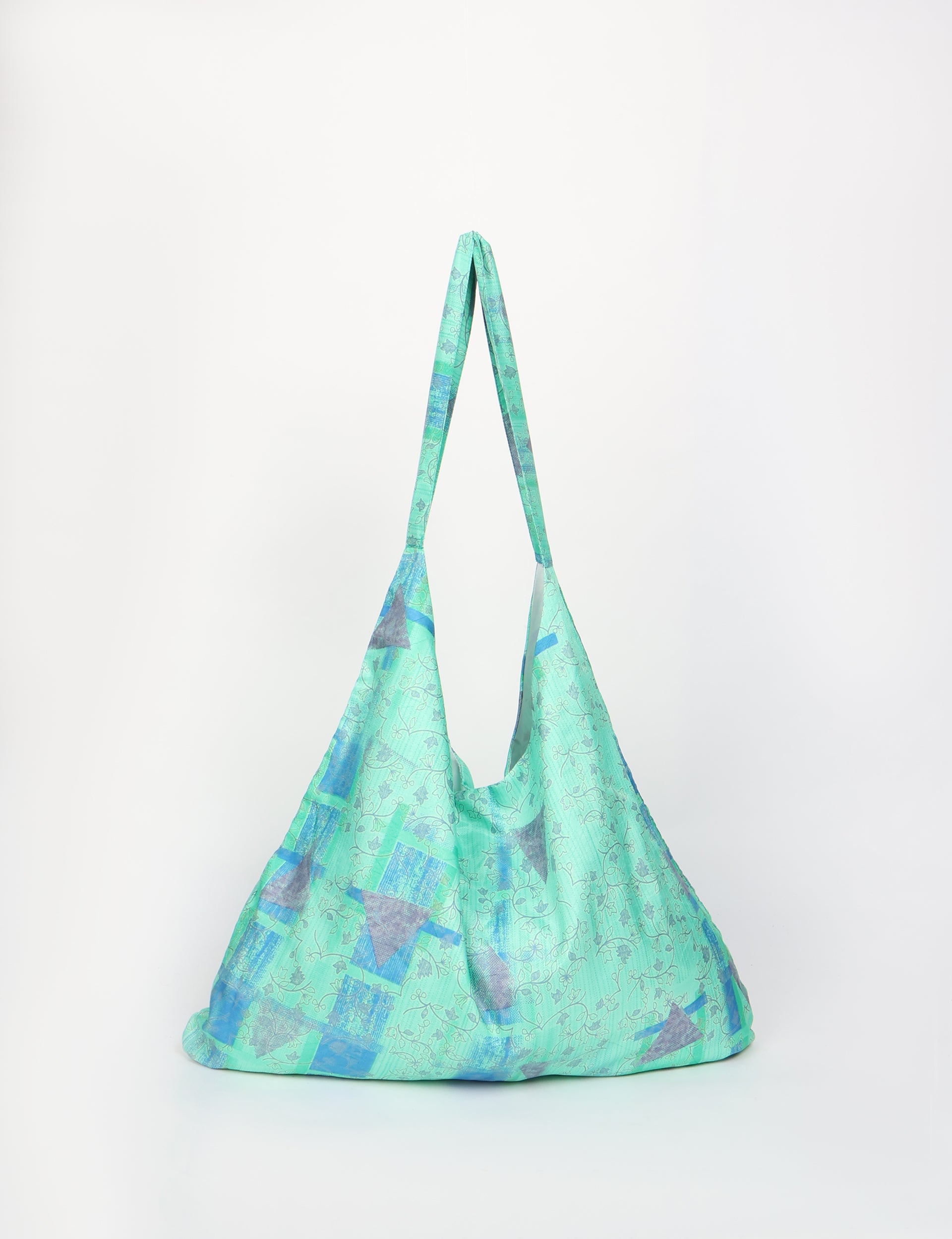 Blue and green tropical patterned trapeze bag with long straps, shown hanging against a white background