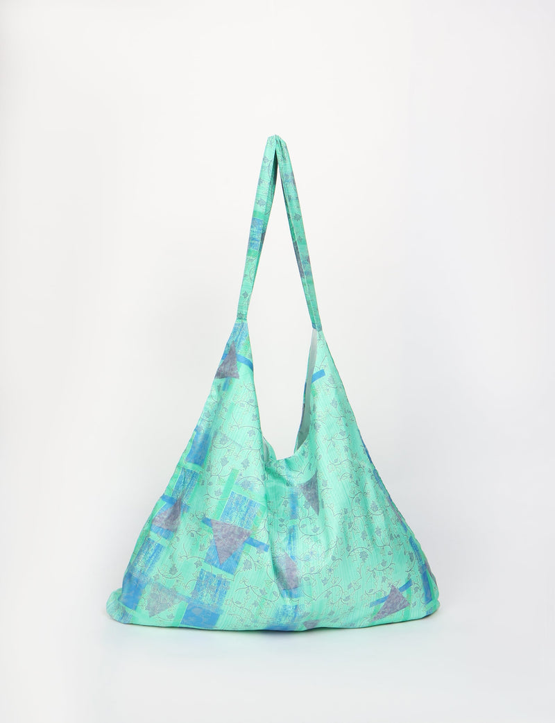 Blue and green tropical patterned trapeze bag with long straps, shown hanging against a white background