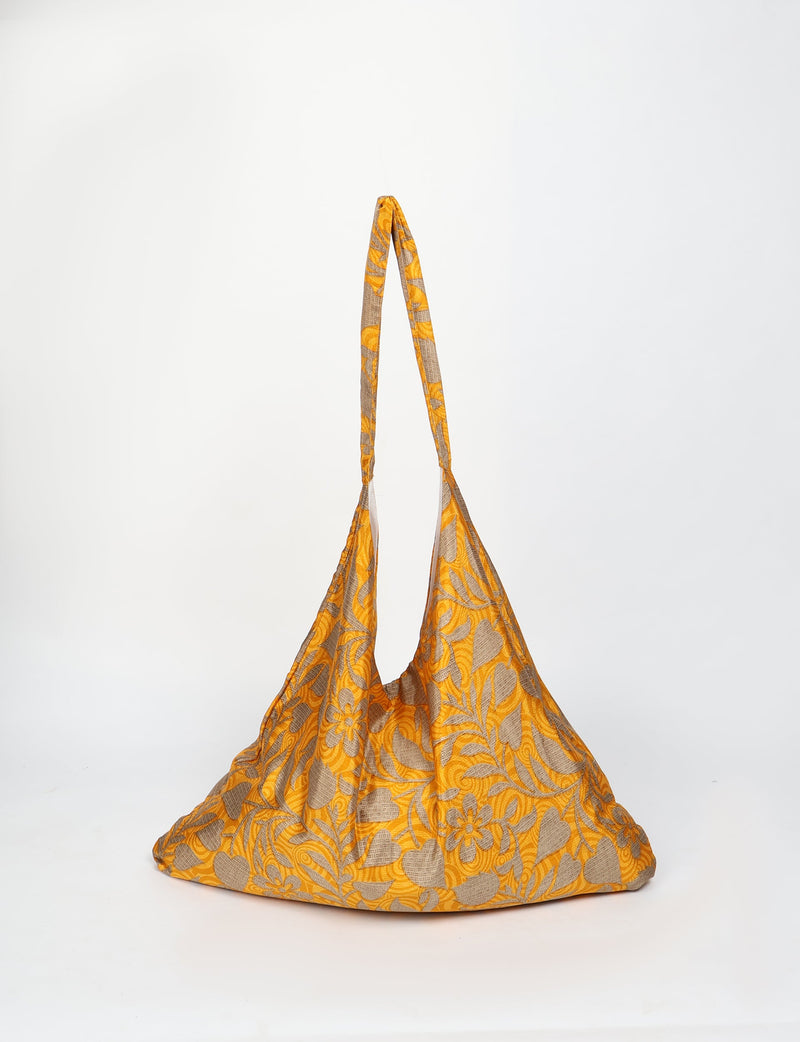 Yellow tropical patterned trapeze bag with long handles, shown hanging against a white background