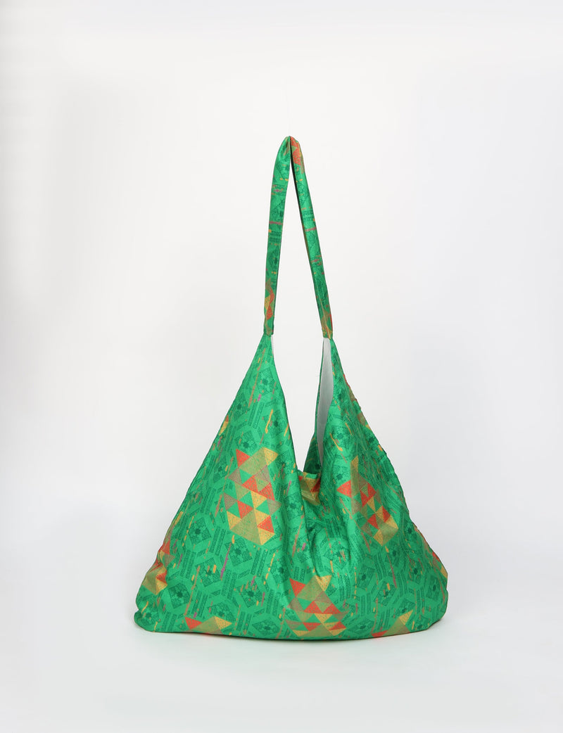Green trapeze bag with geometric pattern in orange and yellow, hanging by its strap against a white background