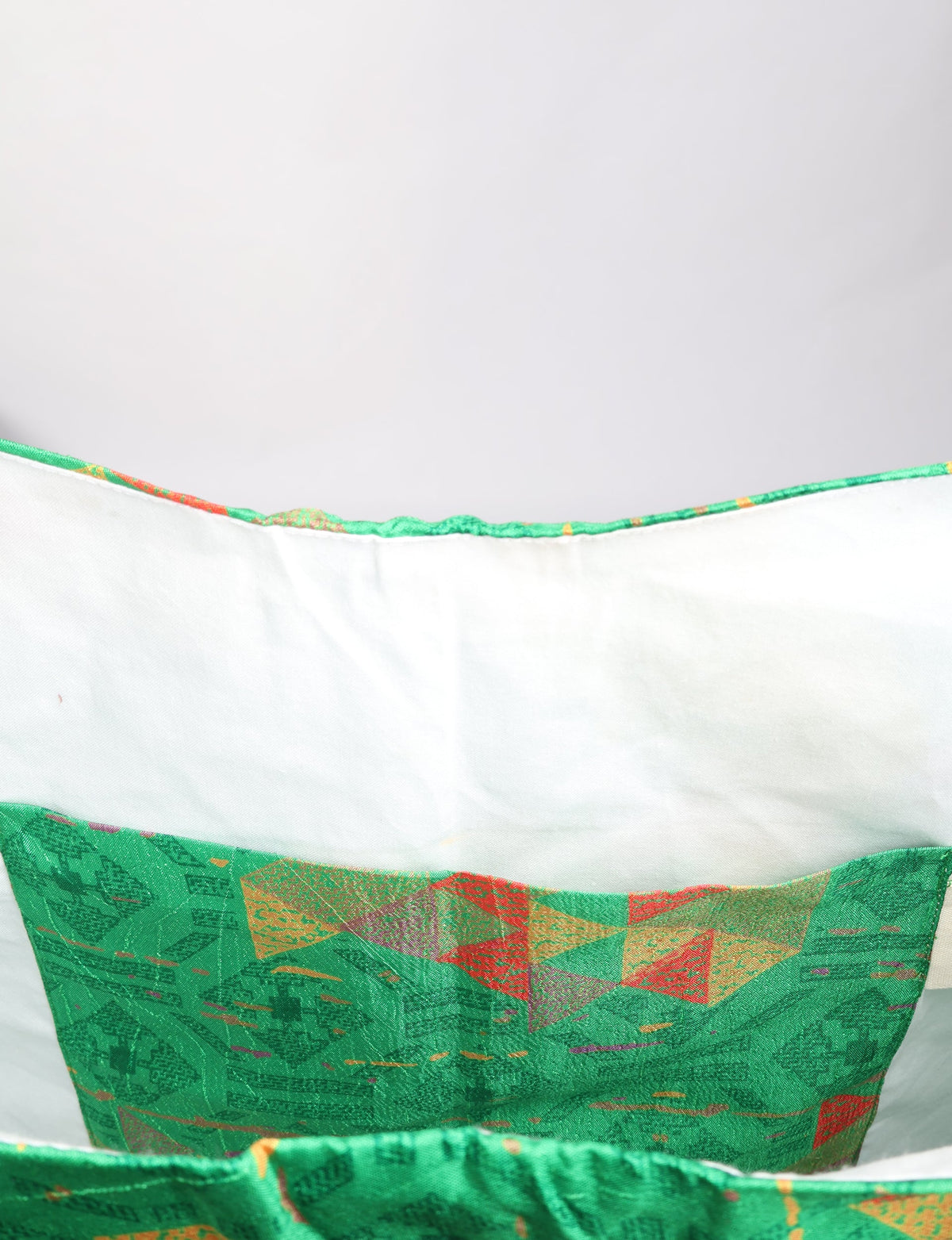 Green geometric patterned trapeze bag interior with white lining and stitched pocket, shown in close-up view