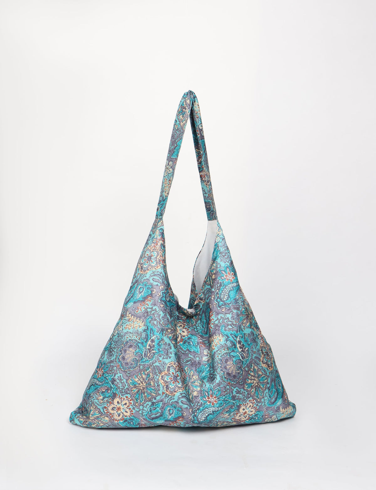 Blue tropical patterned trapeze bag with long handles, shown front view, hanging against white background