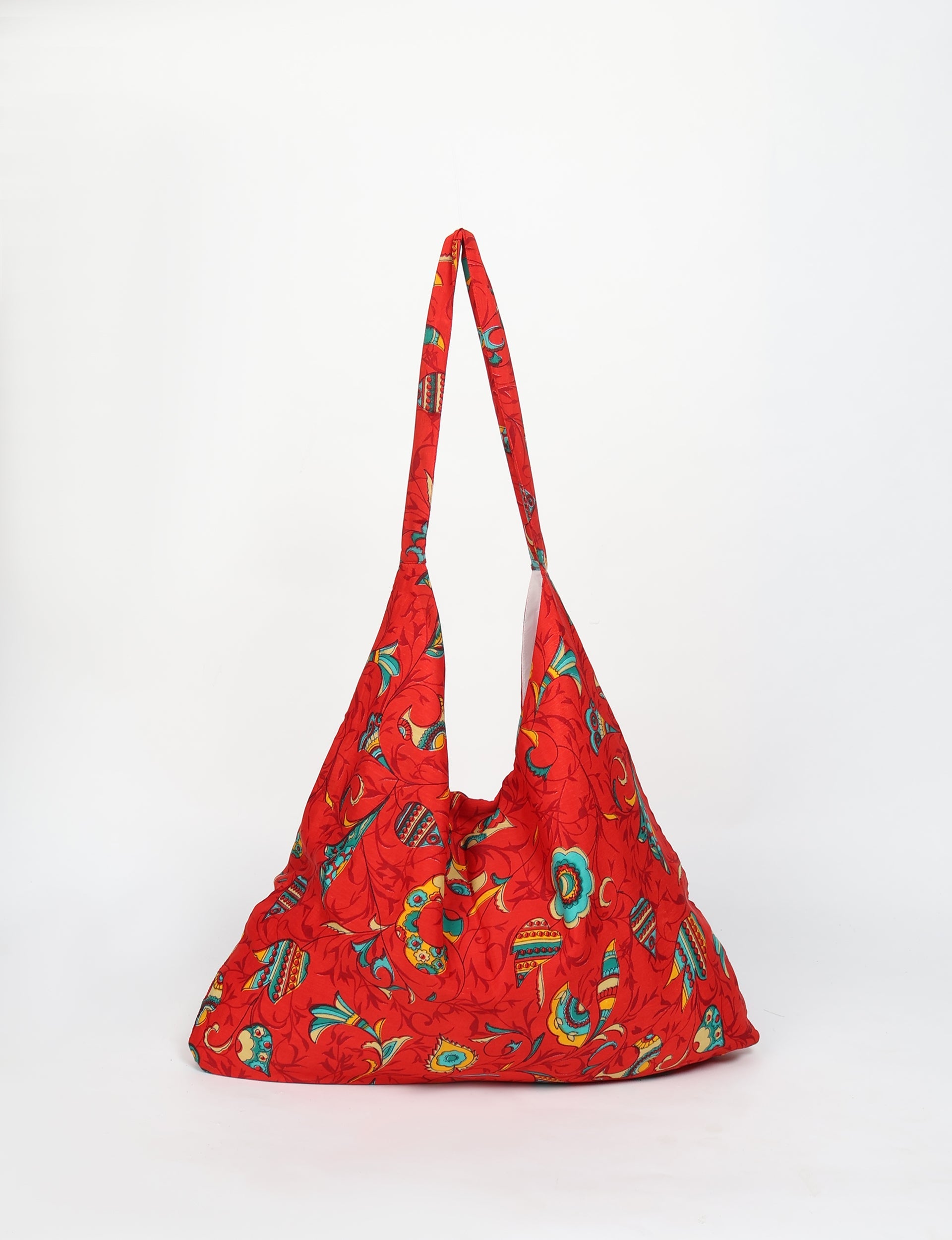Red trapeze bag with tropical multicolor floral and leaf pattern, hanging front view with long strap