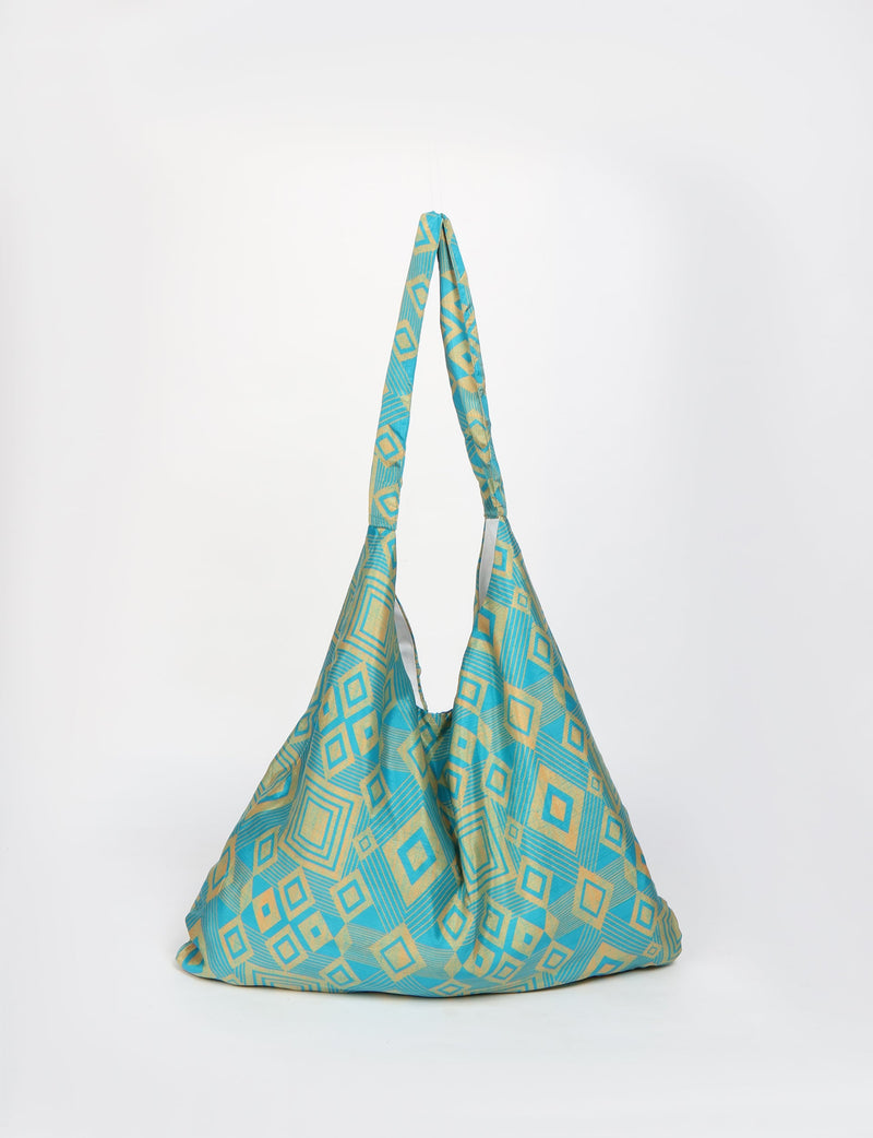 Blue trapeze bag with yellow geometric square and diamond pattern, hanging by its fabric strap against a white background