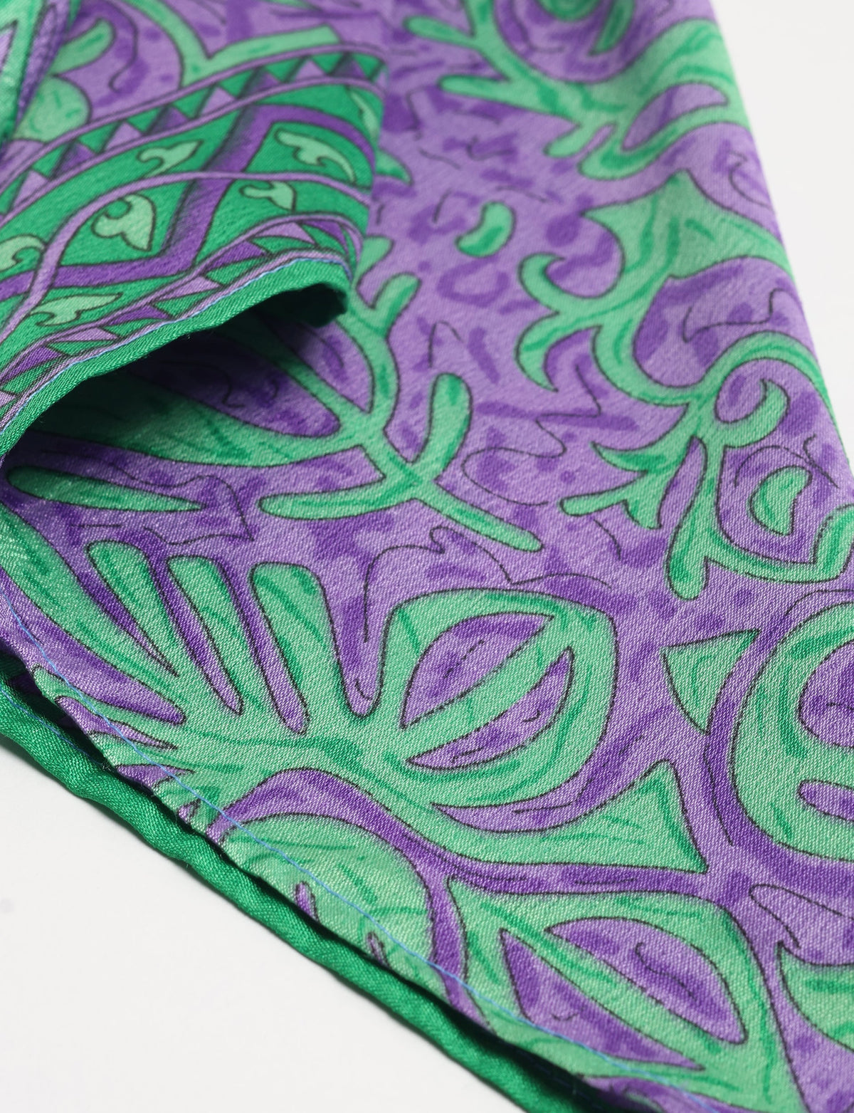 Purple and green tropical patterned foulard fabric with visible stitching on folded edge, close-up view