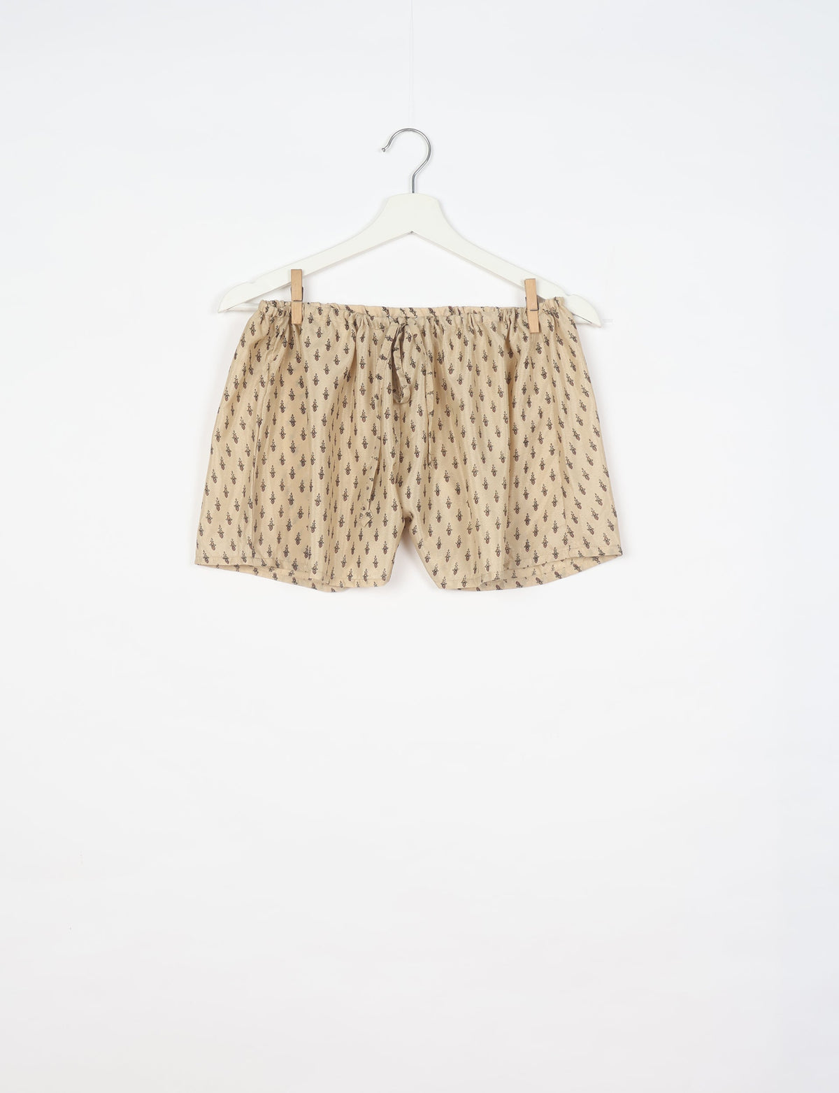 Beige shorts with micro dark brown pattern, elastic waistband with drawstring, hanging on white hanger, front view