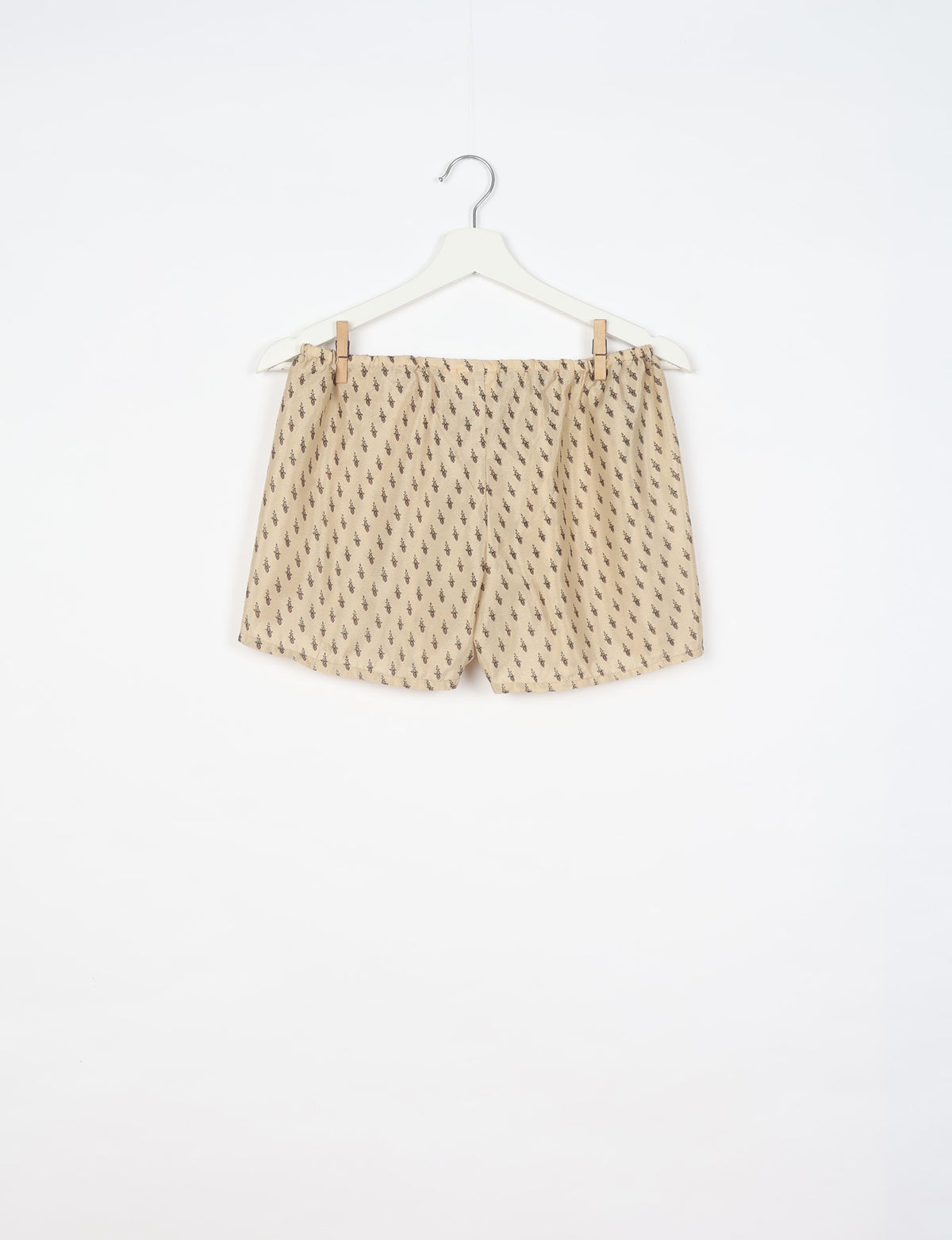 Beige shorts with small dark brown micro pattern, elastic waistband, hanging on white hanger against white background