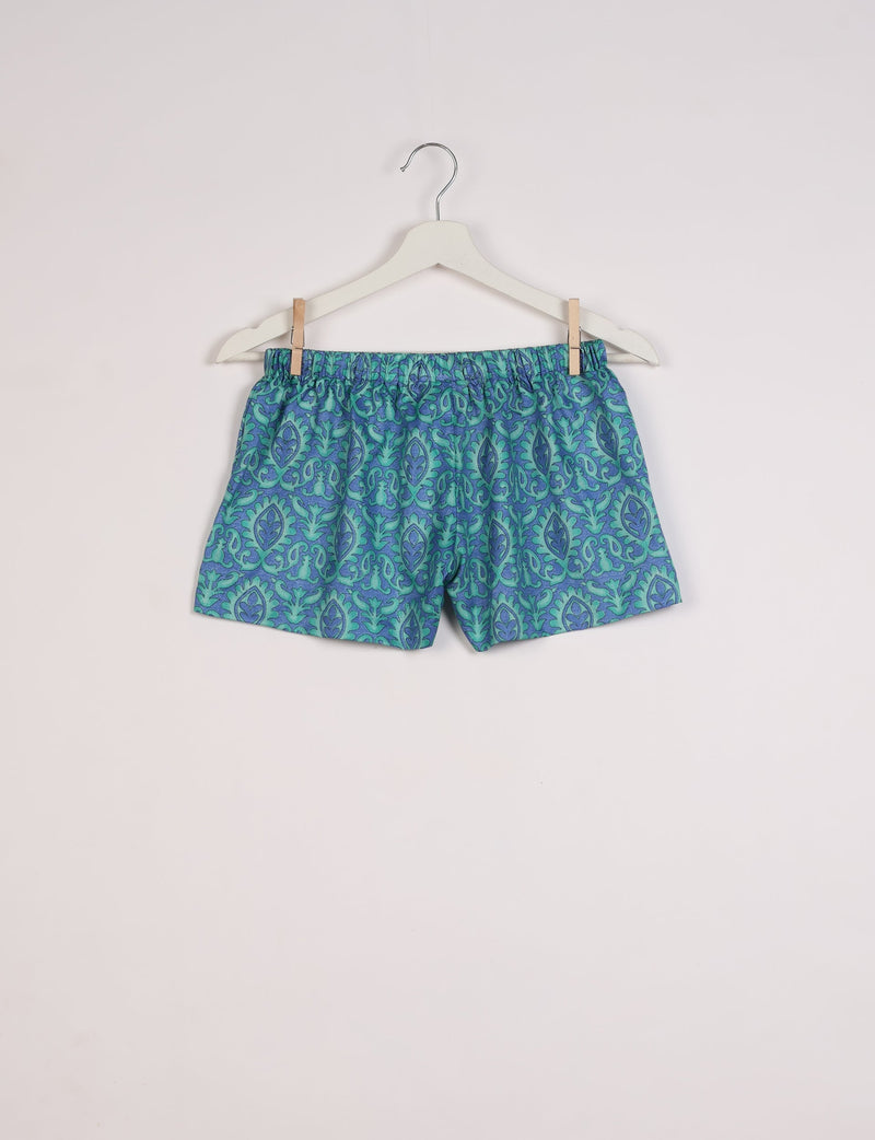 Blue and green Indian ethnic patterned shorts with elastic waistband hanging on white hanger against white background