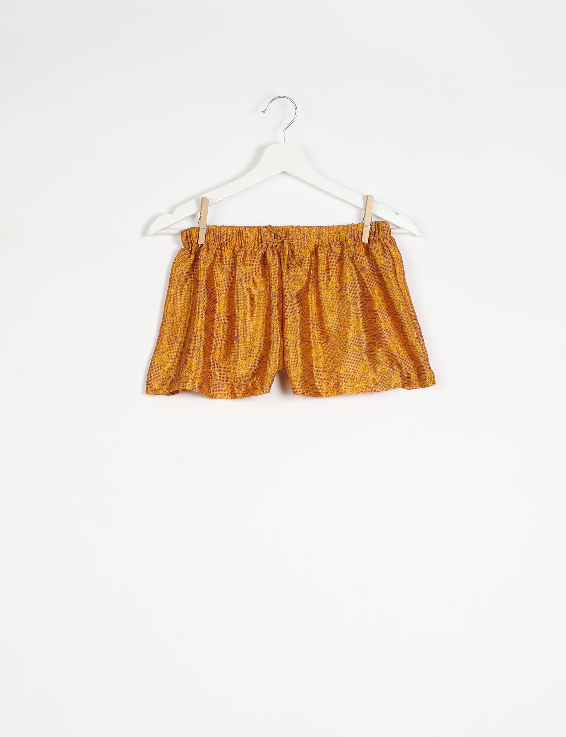Yellow tropical print shorts with elastic waistband and drawstring, hanging on white hanger against white background