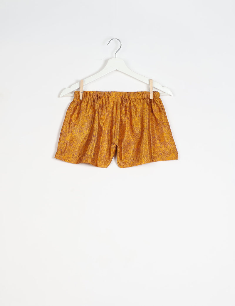 Yellow tropical print shorts with elastic waistband hanging on white hanger against white background