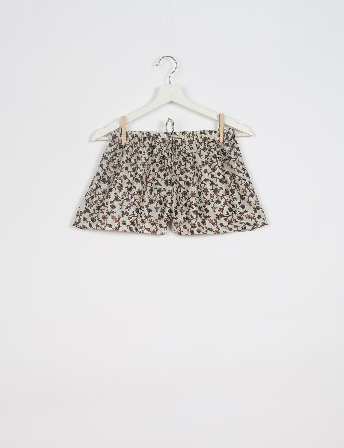 Beige shorts with brown and blue floral print, elastic waistband with drawstring, hanging on white hanger against white background