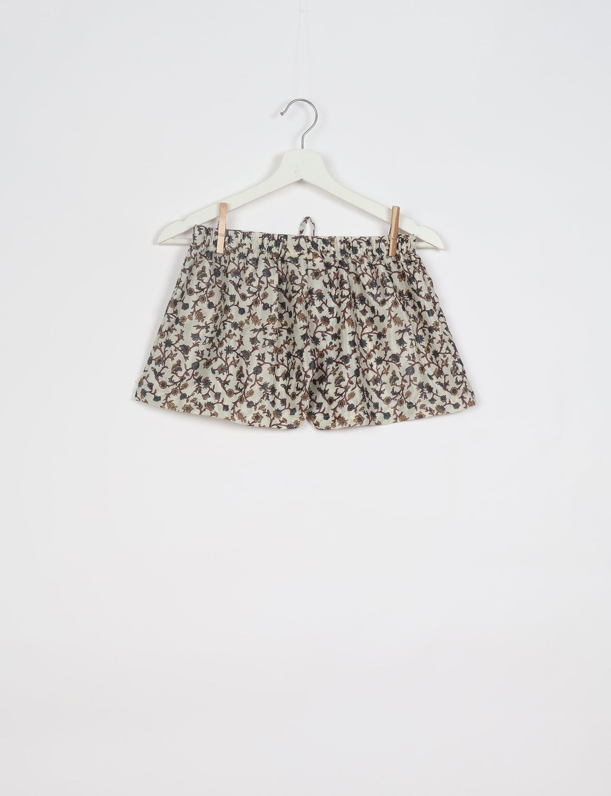 Beige shorts with brown and black floral print, elastic waistband, hanging on white hanger against white background
