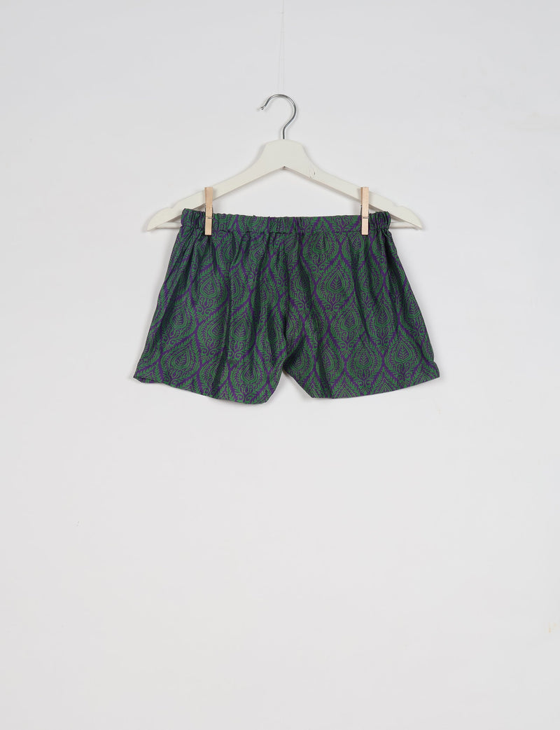 Purple shorts with green leaf pattern, elastic waistband, hanging on white hanger against white background