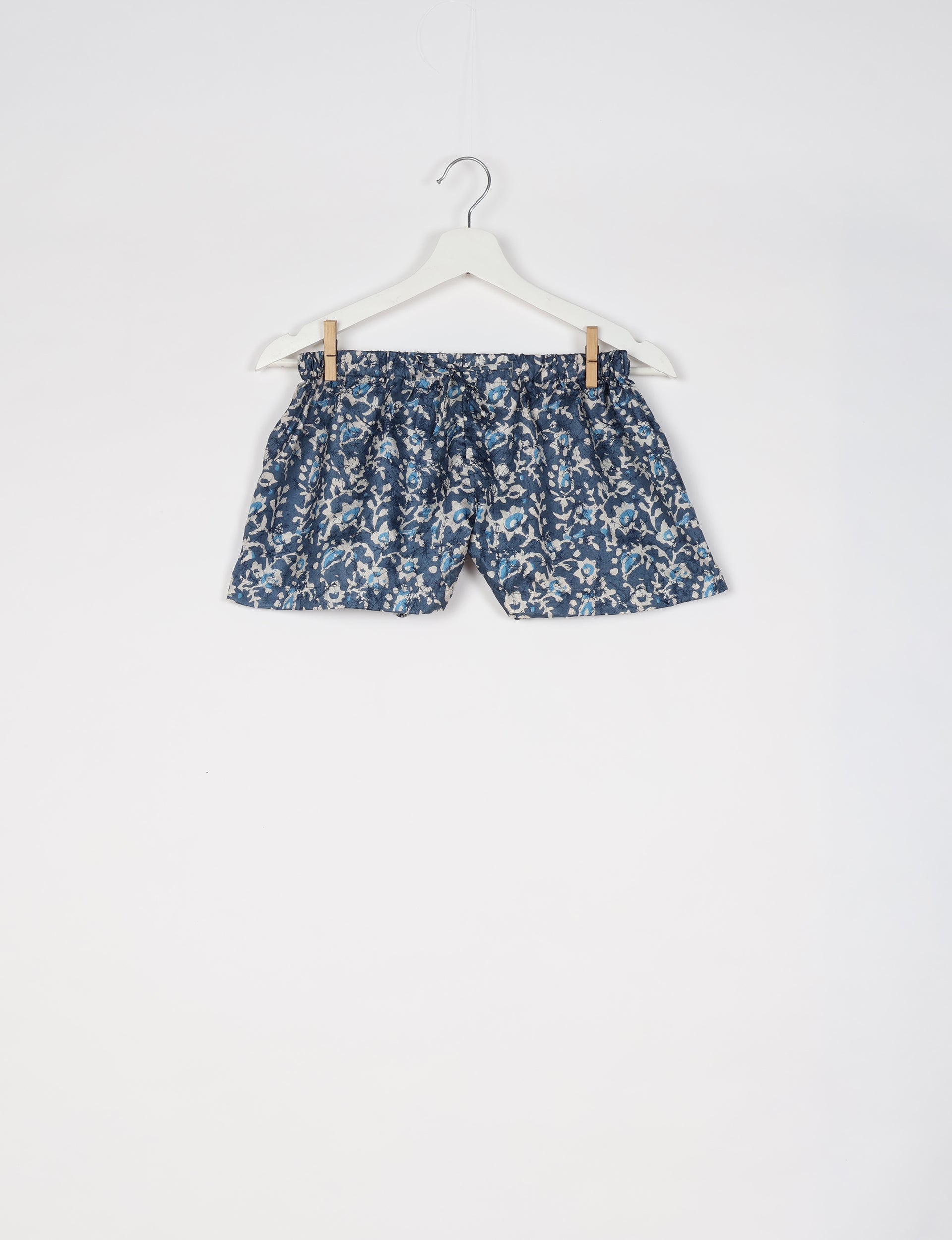 Blue tropical print shorts with elastic waistband hanging on white hanger against white background