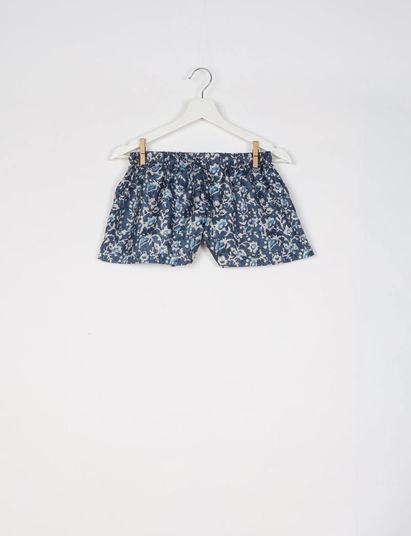 Blue tropical print shorts with elastic waistband hanging on white hanger against white background