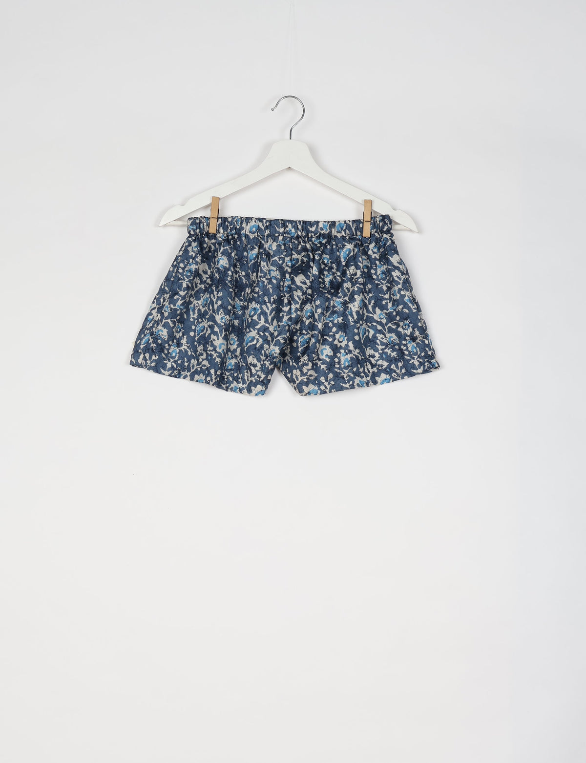 Blue tropical print shorts with elastic waistband hanging on white hanger against white background