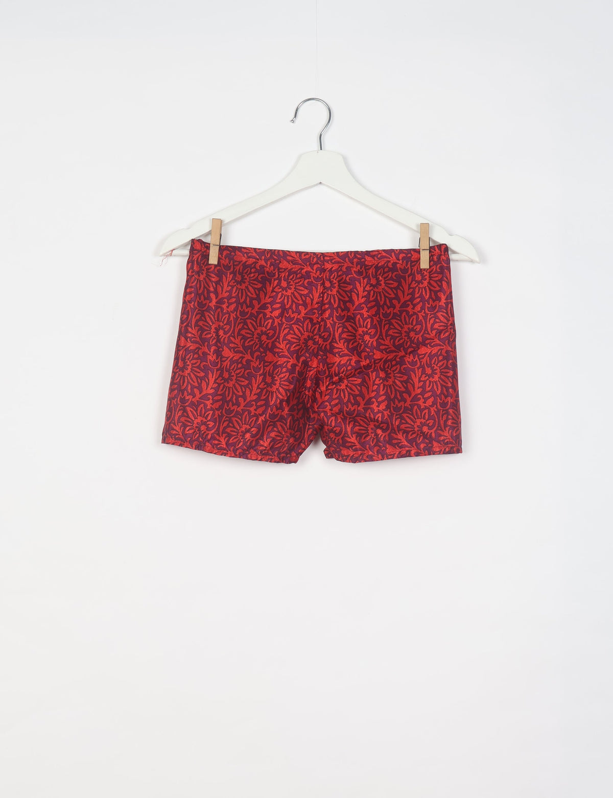 Red tropical print shorts with floral pattern hanging on white hanger against white background