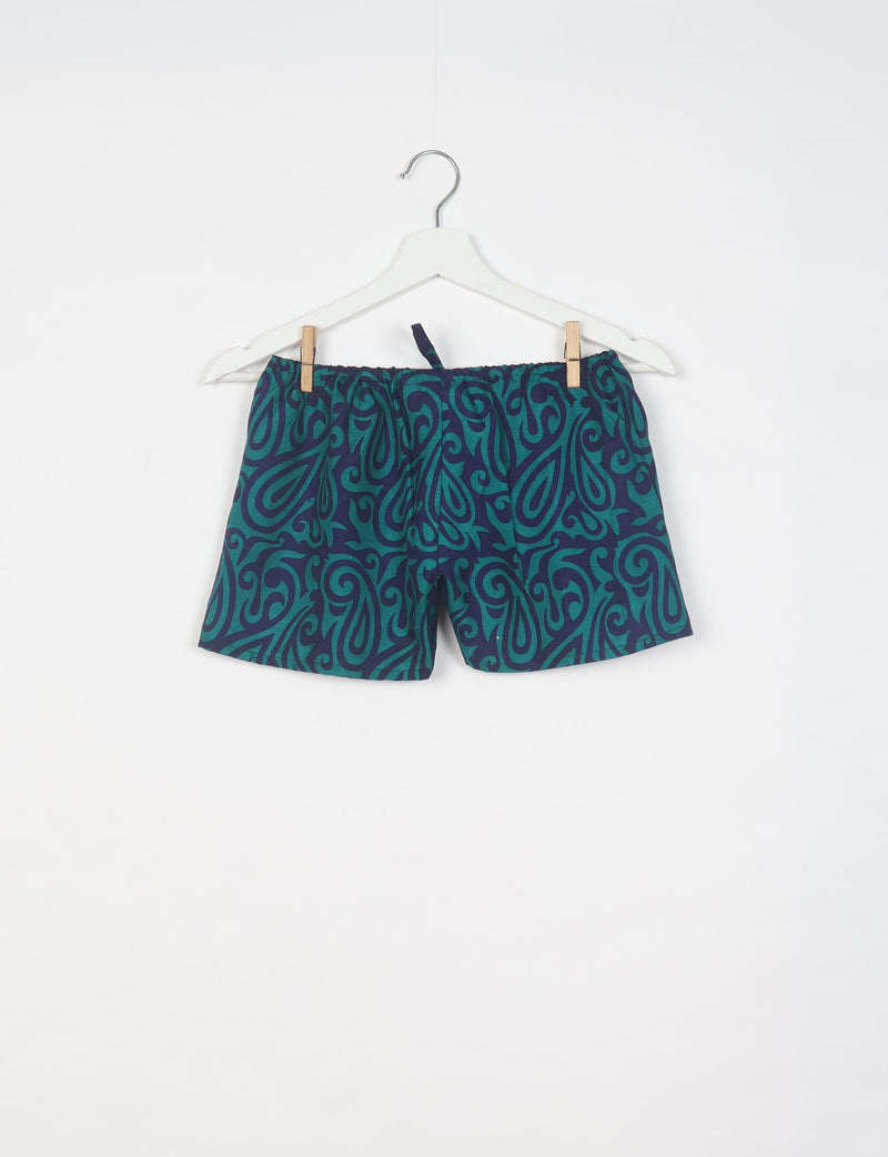 Blue paisley patterned shorts with elastic waistband hanging on white hanger against white background