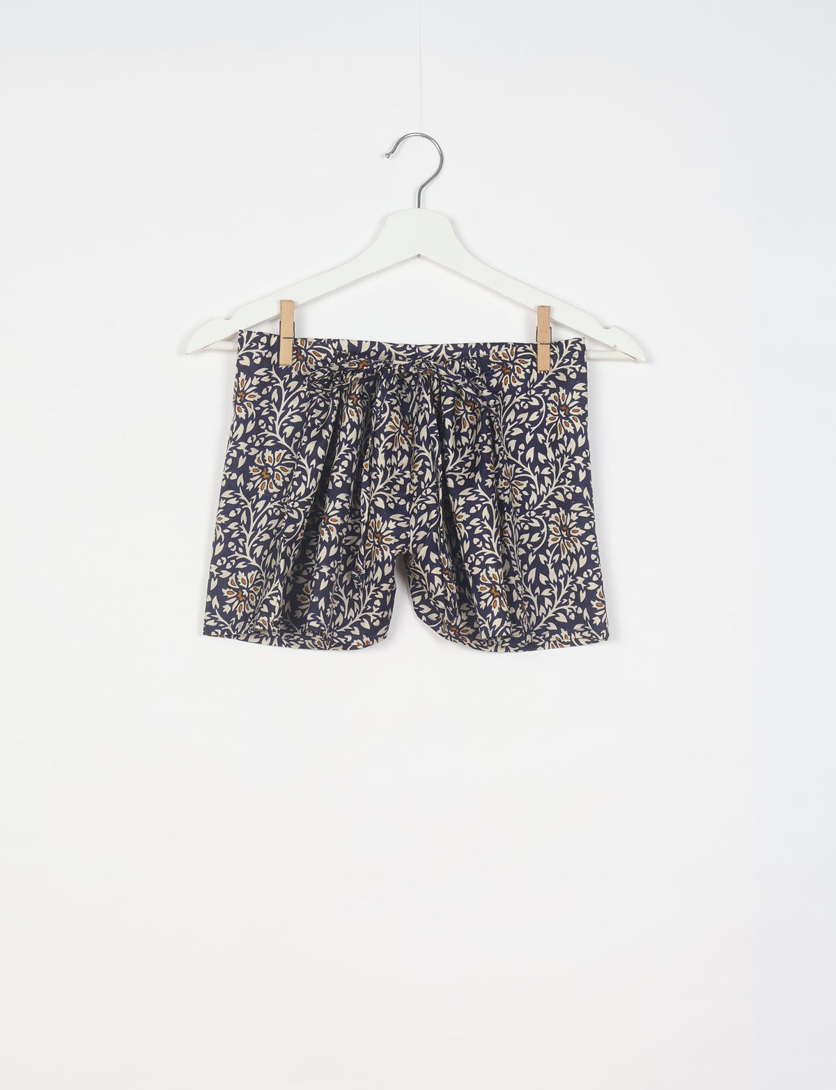 Black tropical print shorts with beige and brown floral pattern, elastic waistband, and front tie, hanging on white hanger