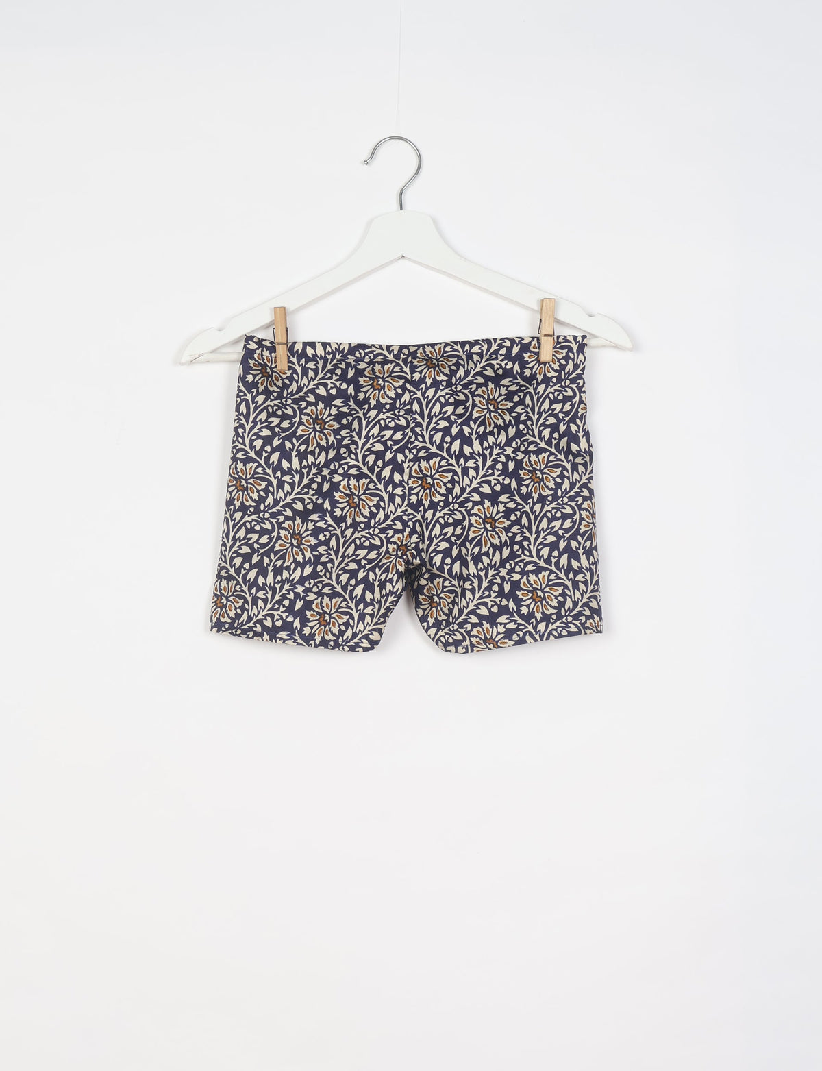 Black shorts with beige and brown tropical floral print hanging on a white hanger against a white background