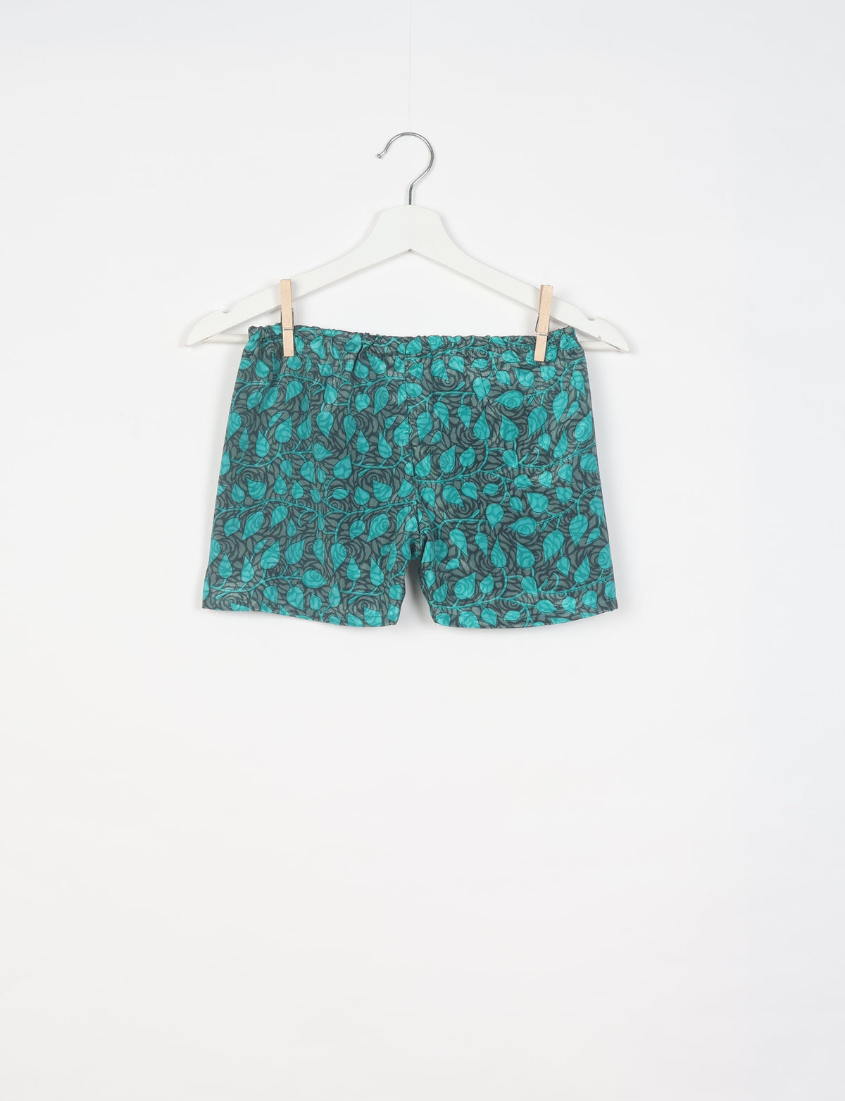 Grey shorts with teal leaf pattern hanging on white hanger against white background