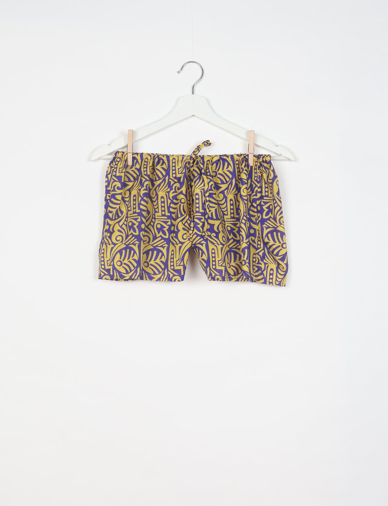 Purple and yellow tropical print shorts with elastic waistband and drawstring, hanging on white hanger against white background