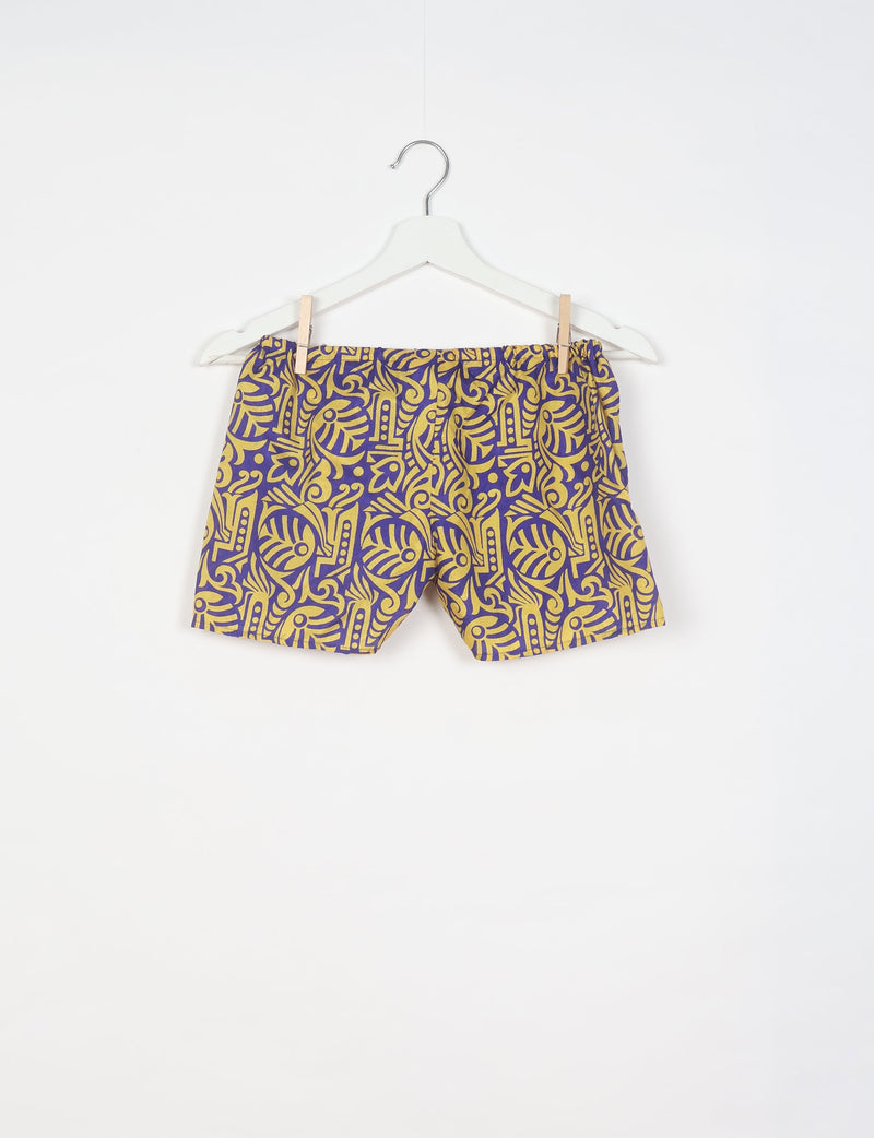 Purple shorts with yellow tropical abstract pattern hanging on white hanger against white background