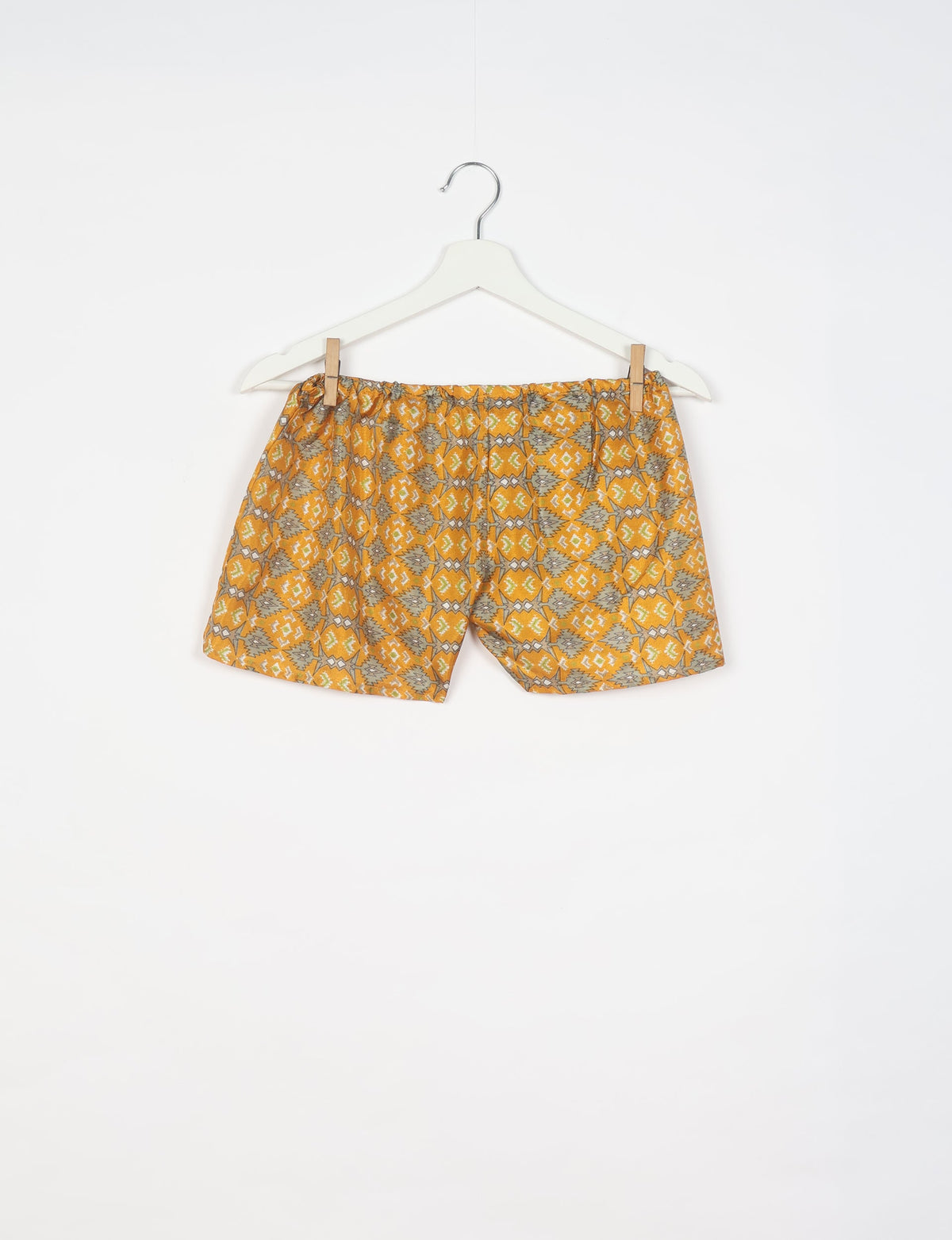 Yellow shorts with gray and white geometric pattern hanging on white hanger against white background