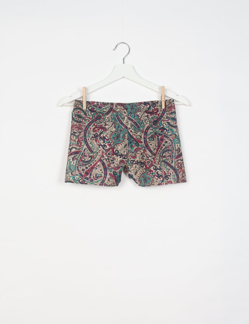 Beige shorts with multicolor tropical paisley pattern hanging on white hanger against white background