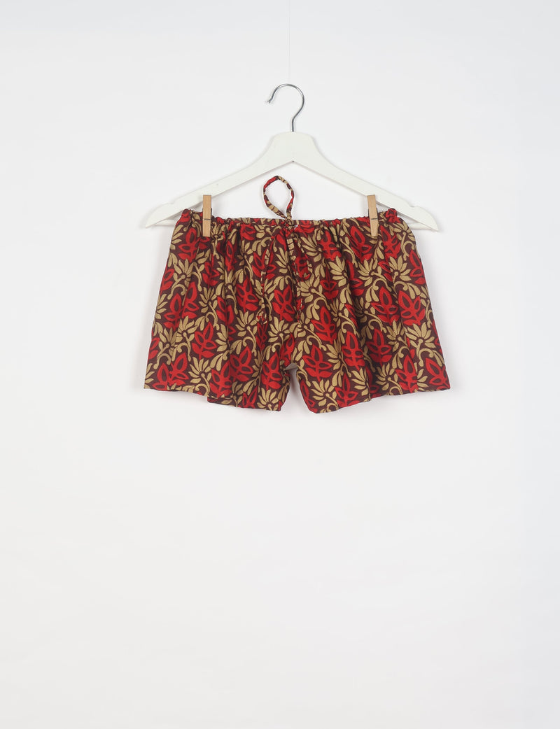 Red and beige leaf-patterned shorts with elastic waistband and drawstring, hanging on white hanger against white background