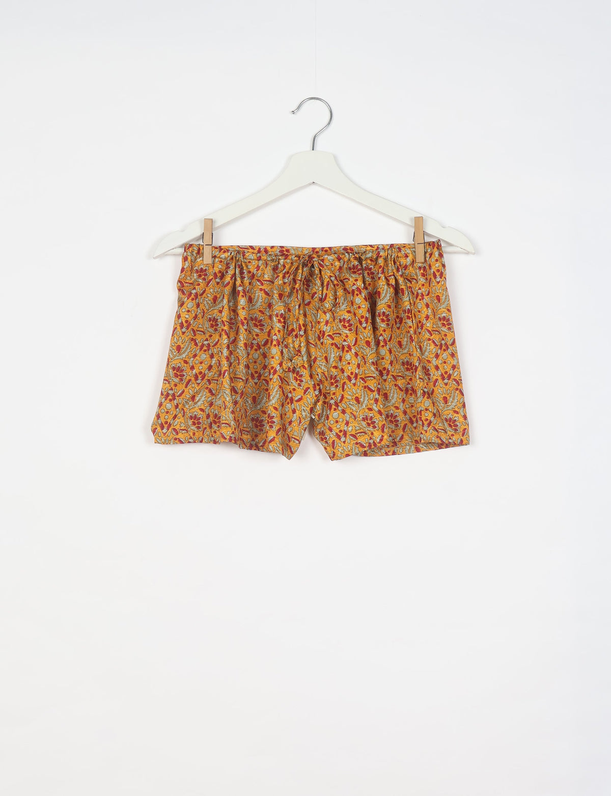 Yellow tropical patterned shorts with elastic waistband hanging on white hanger against white background