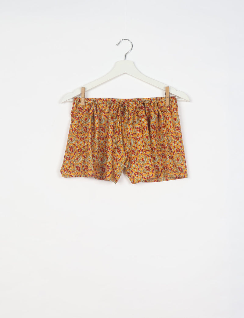 Yellow tropical patterned shorts with elastic waistband hanging on white hanger against white background
