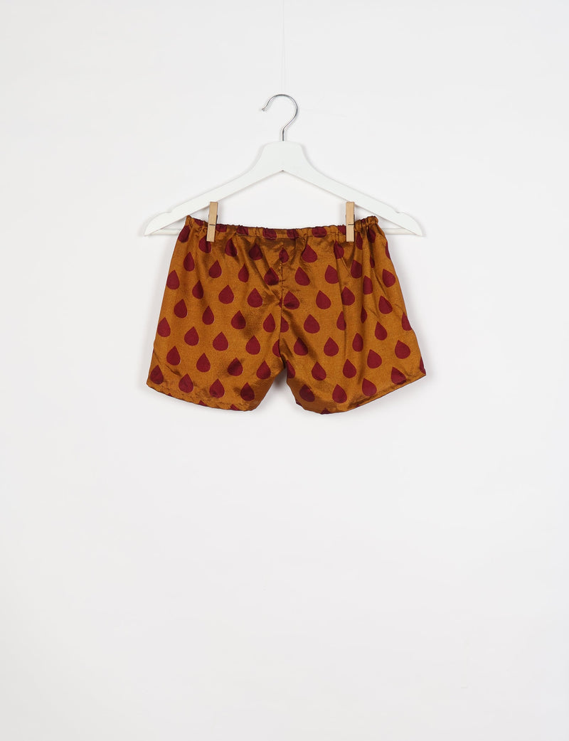 Yellow shorts with maroon teardrop pattern, elastic waistband, hanging on white hanger against white background
