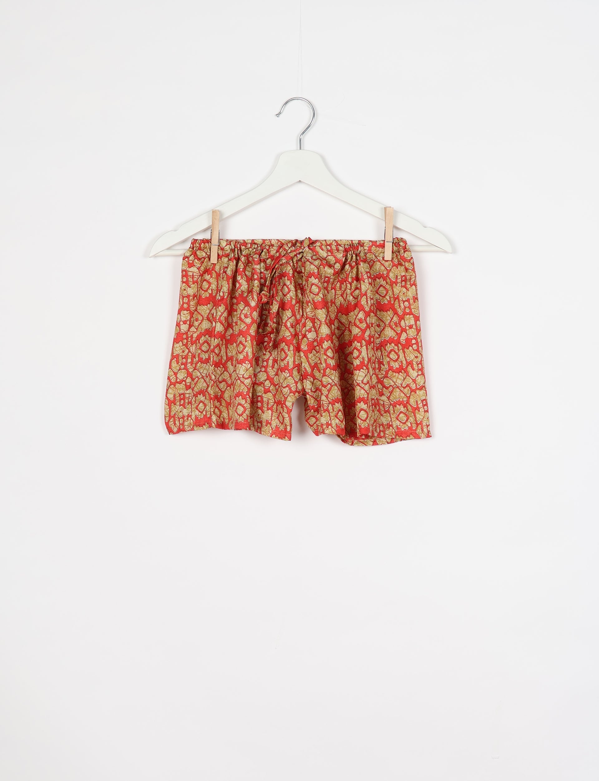 Orange Indian ethnic shorts with an elastic waistband and drawstring, featuring a traditional patterned print, hanging on a white hanger