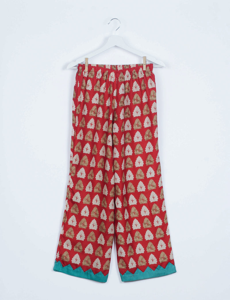 Red floral print pajama pants with elastic waistband and teal zigzag hem, hanging on white hanger against white background