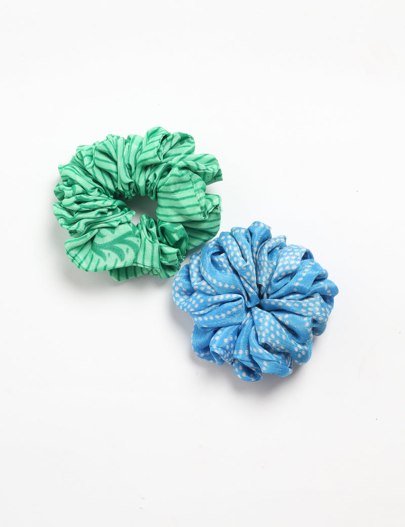 Set of two fabric scrunchies, one green with abstract stripes and one blue with white polka dots, flat lay on white background