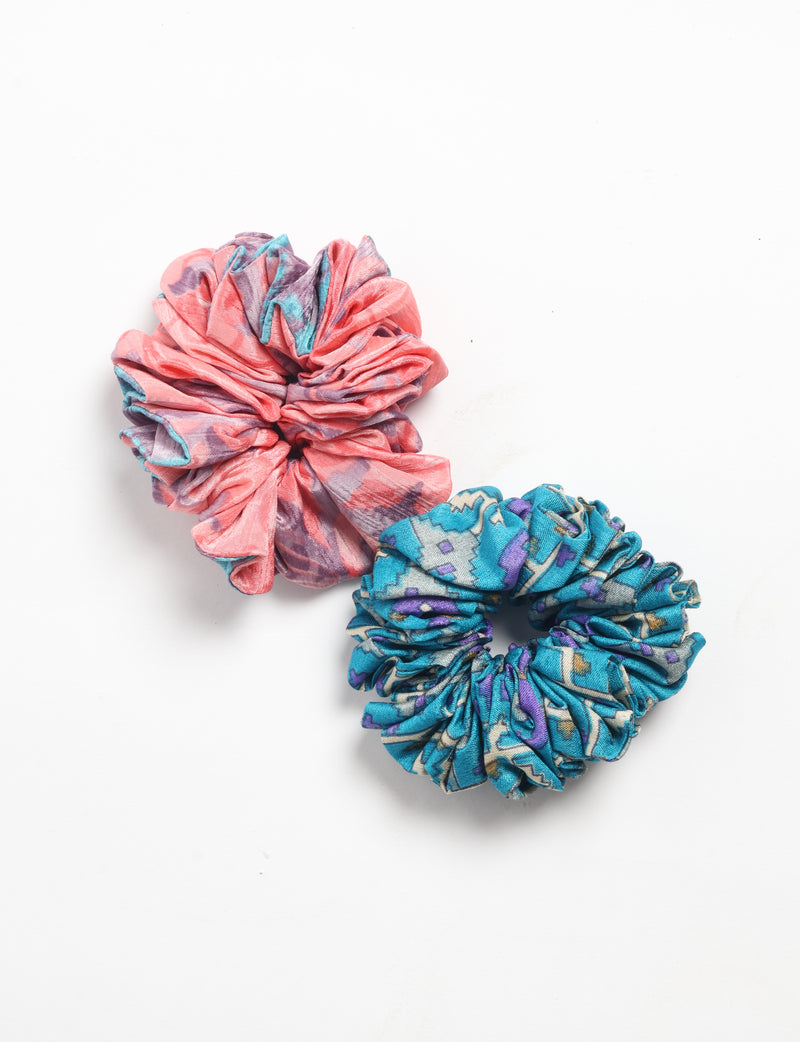 Set of two fabric scrunchies with abstract patterns, one coral with purple and blue, one blue with geometric shapes, flat lay