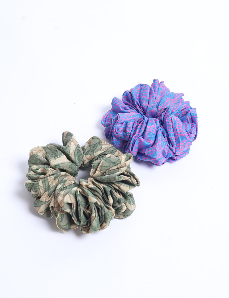 Set of two assorted scrunchies, one blue with pink pattern and one beige with green leaf pattern, flat lay on white background