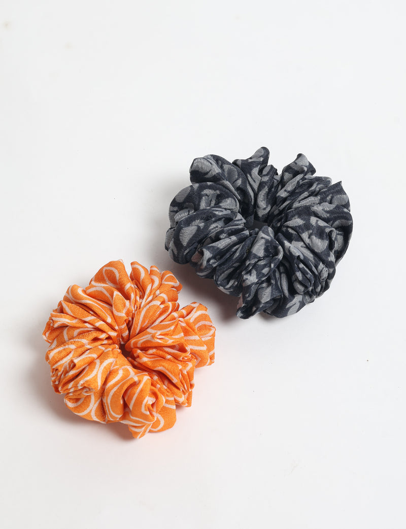 Set of two scrunchies, one orange with white swirl pattern and one black and gray camouflage pattern, flat lay on white background