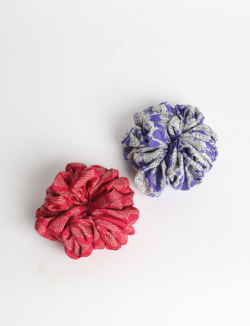 Set of two fabric scrunchies, one turquoise with beige abstract spots, one red with white linear pattern, flat lay on white