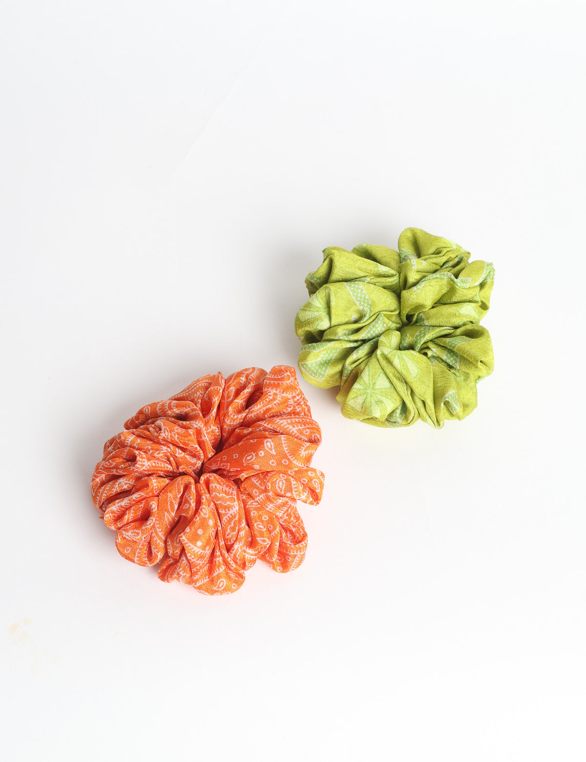 Set of two fabric scrunchies, one turquoise with beige abstract spots, one red with white linear pattern, flat lay on white
