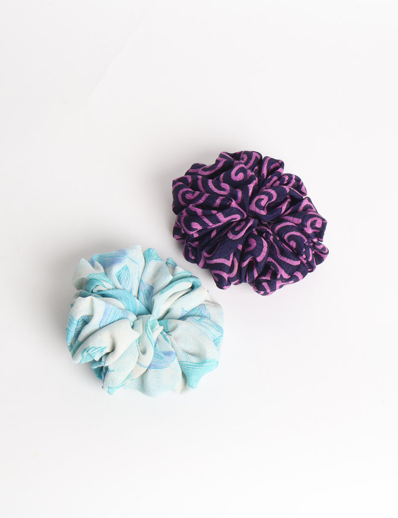 Set of two fabric scrunchies, one turquoise with beige abstract spots, one red with white linear pattern, flat lay on white